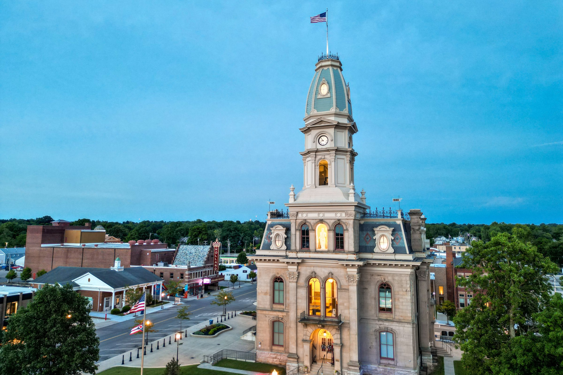 The Logan County Courthouse in downtown Bellefontaine, Ohio, at dusk, with the Holland Theatre marquee at left.
