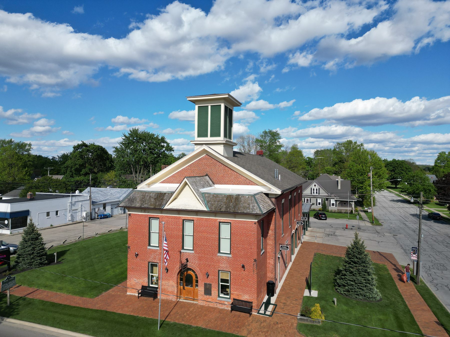 West Liberty Village Town Hall, a red-brick building with a white cupola, flagpole and brick plaza in front