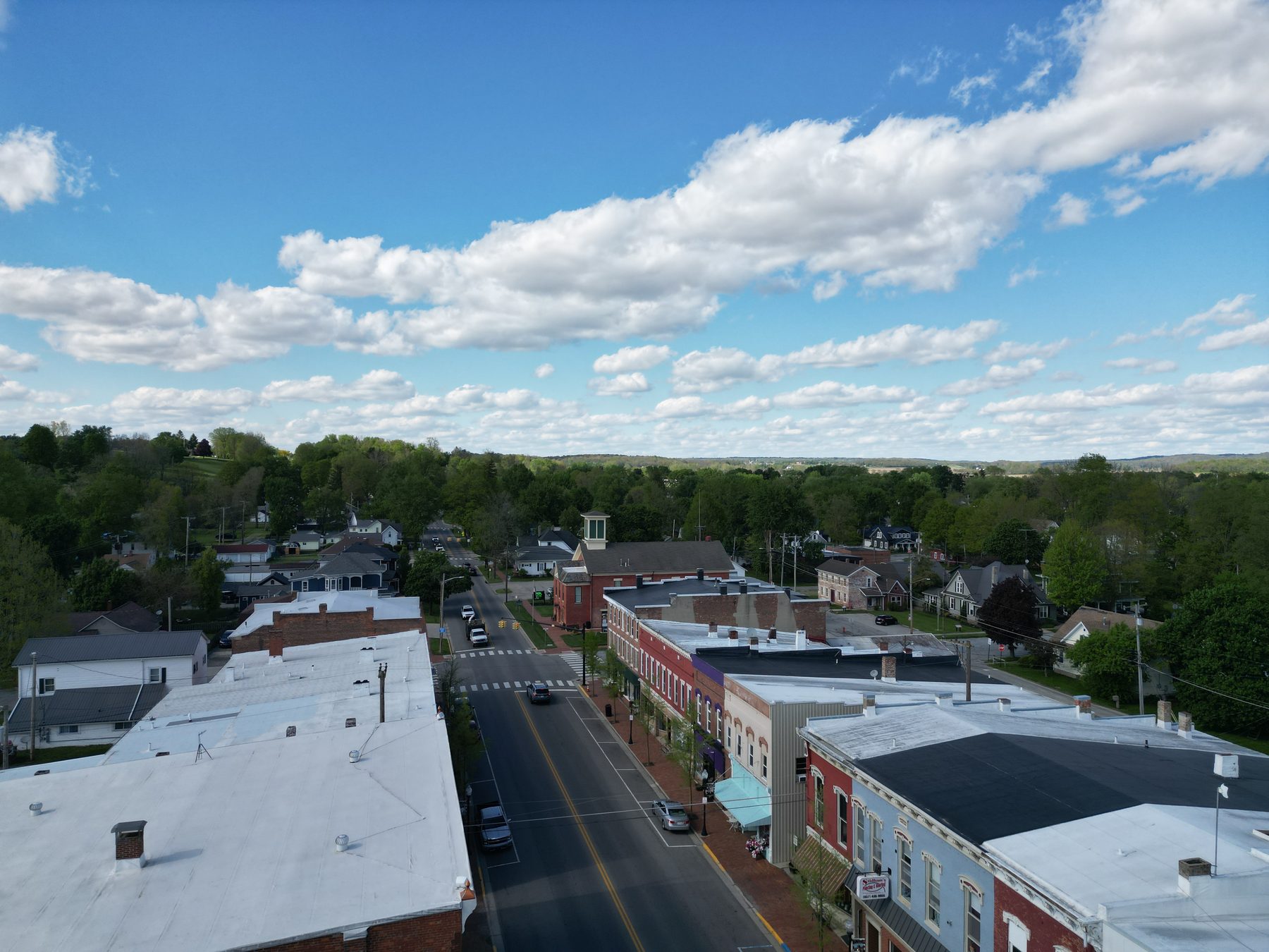 The downtown block from the air, storefronts on both sides of the street with houses and trees behind them