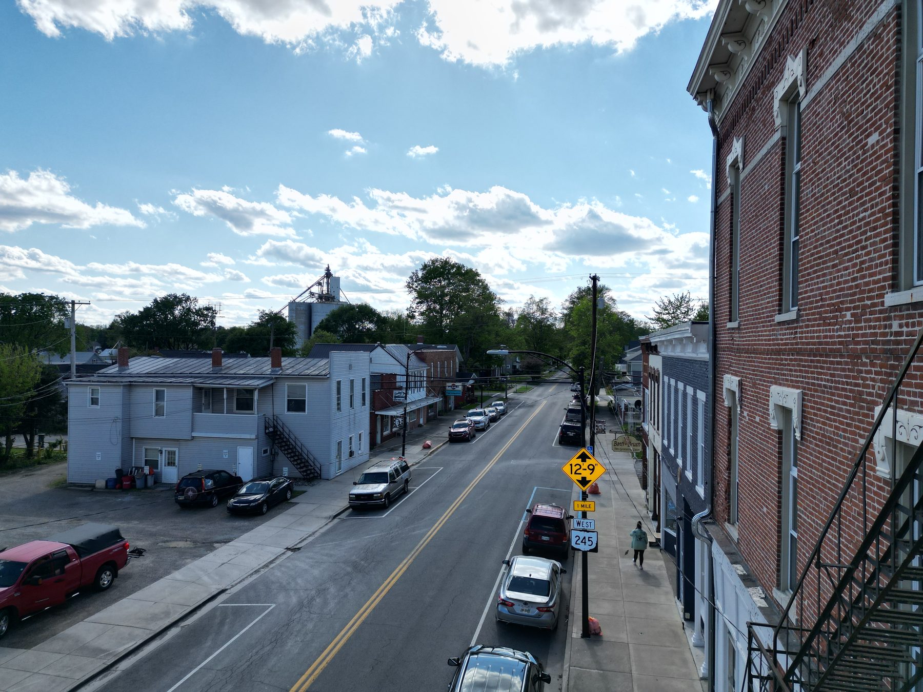 Looking down the main street between the downtown buildings, with parked cars, US-68 and SR-245 route signs and the grain elevator beyond
