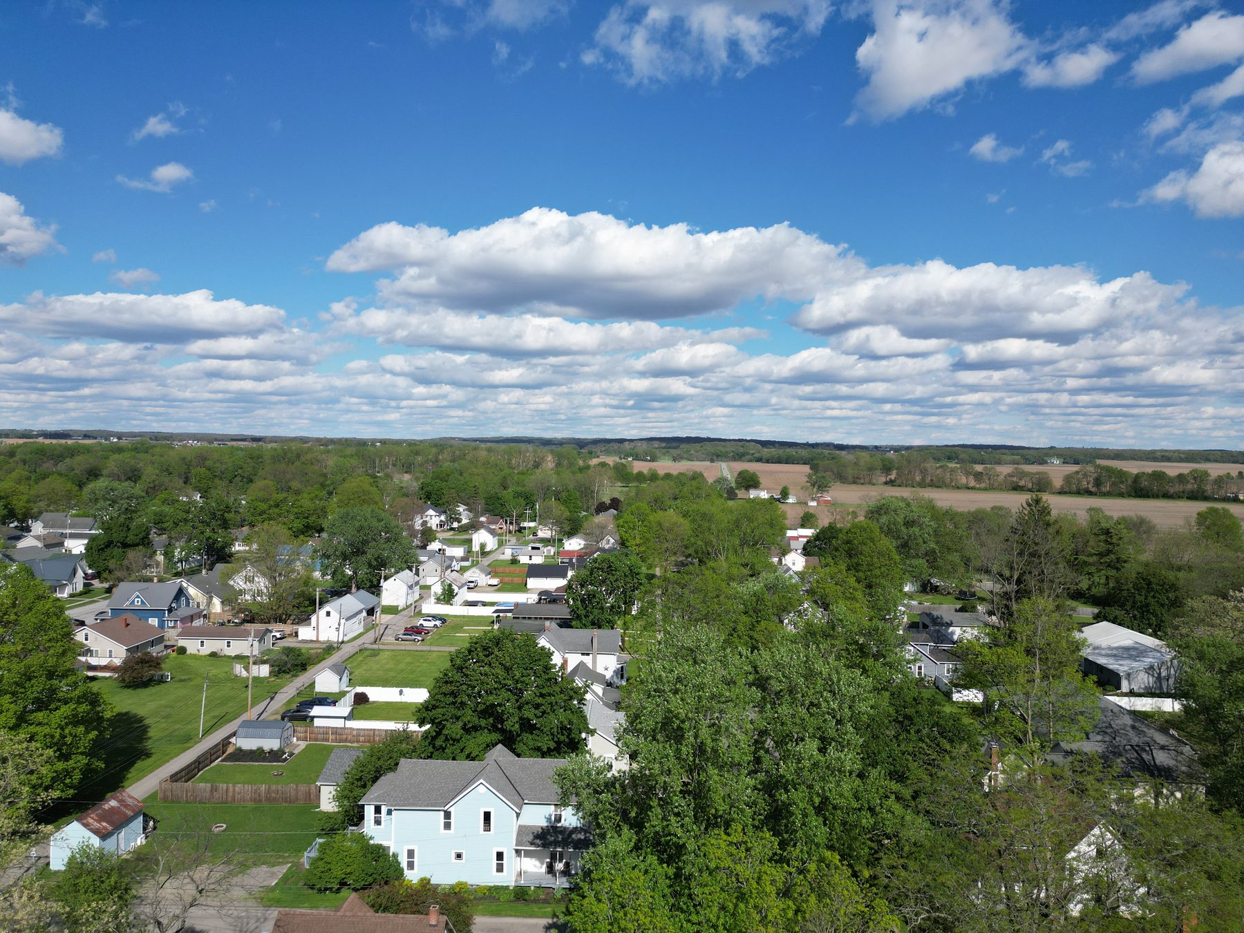 A West Liberty residential street from the air, houses on tree-lined lots with fields at the village edge
