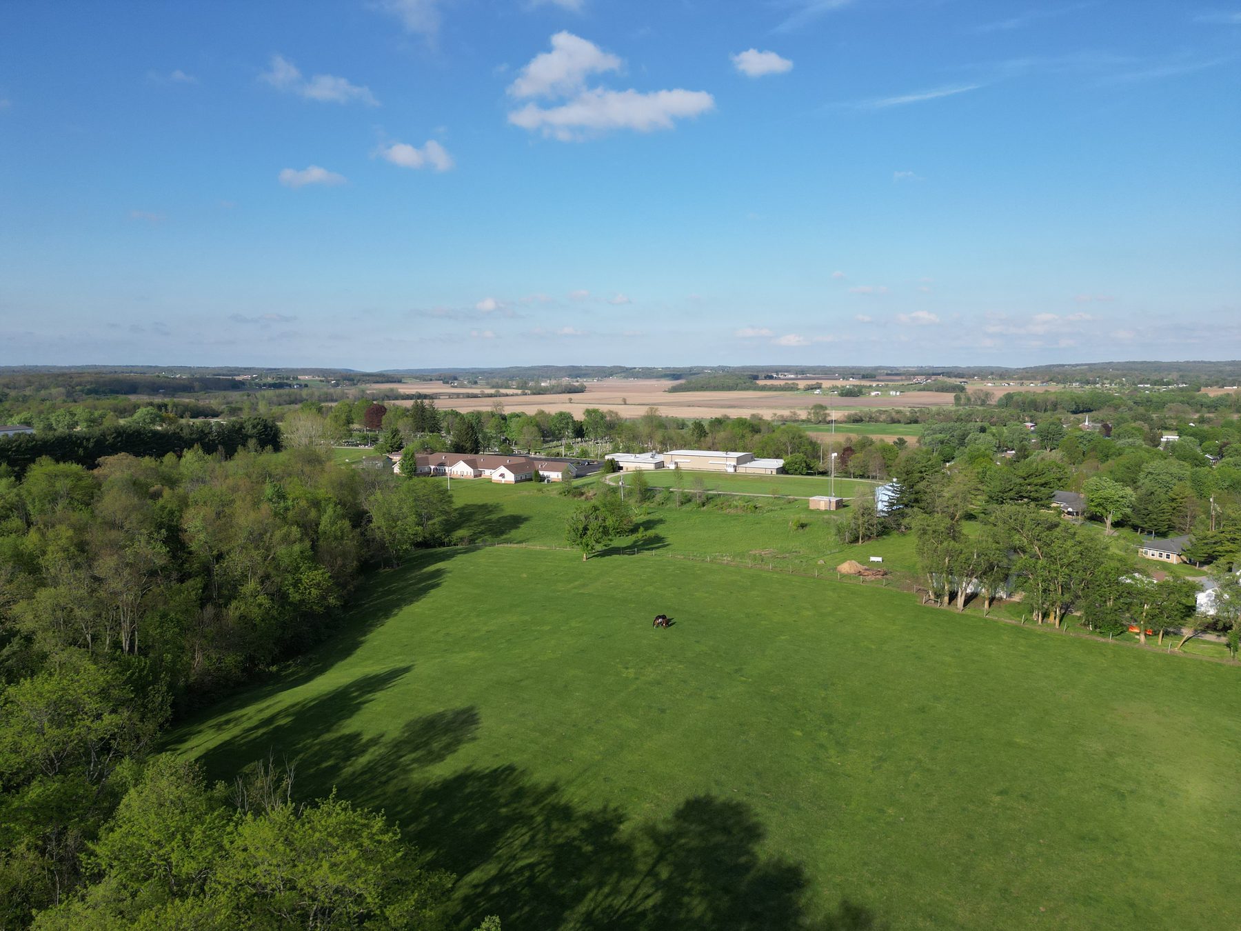 Farmland at the village edge, open pasture and cropland running out to woods and the horizon