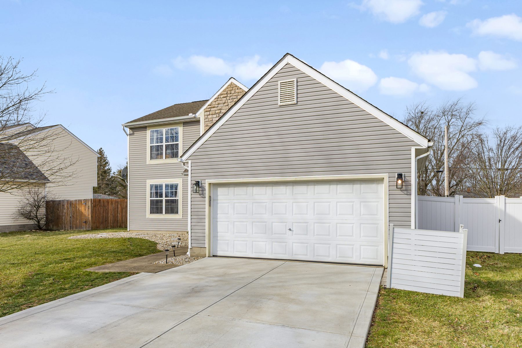 Front of the house from the end of the driveway, showing the garage doors and the white vinyl fence along the side yard