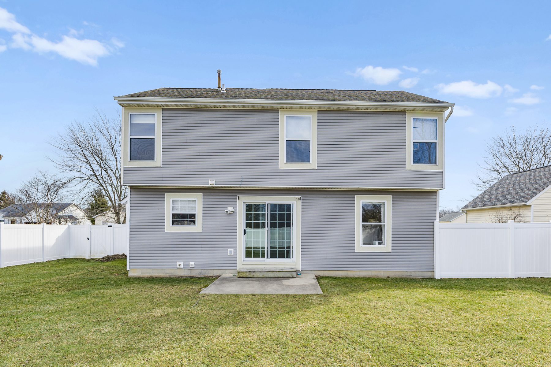 Rear elevation of the house with sliding glass doors onto a concrete patio and windows across both floors