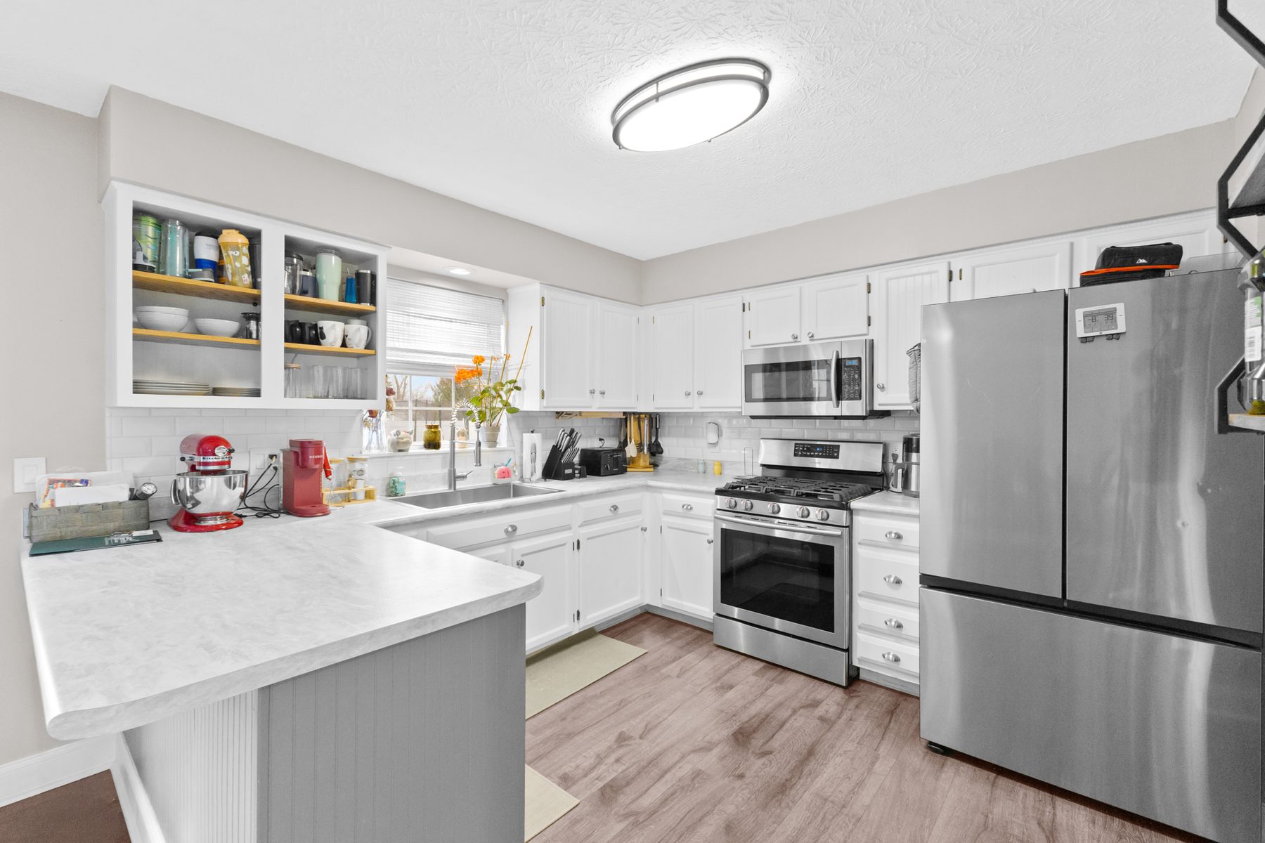 Kitchen with white cabinetry, open shelving, light stone-look counters, a stainless gas range and a stainless refrigerator