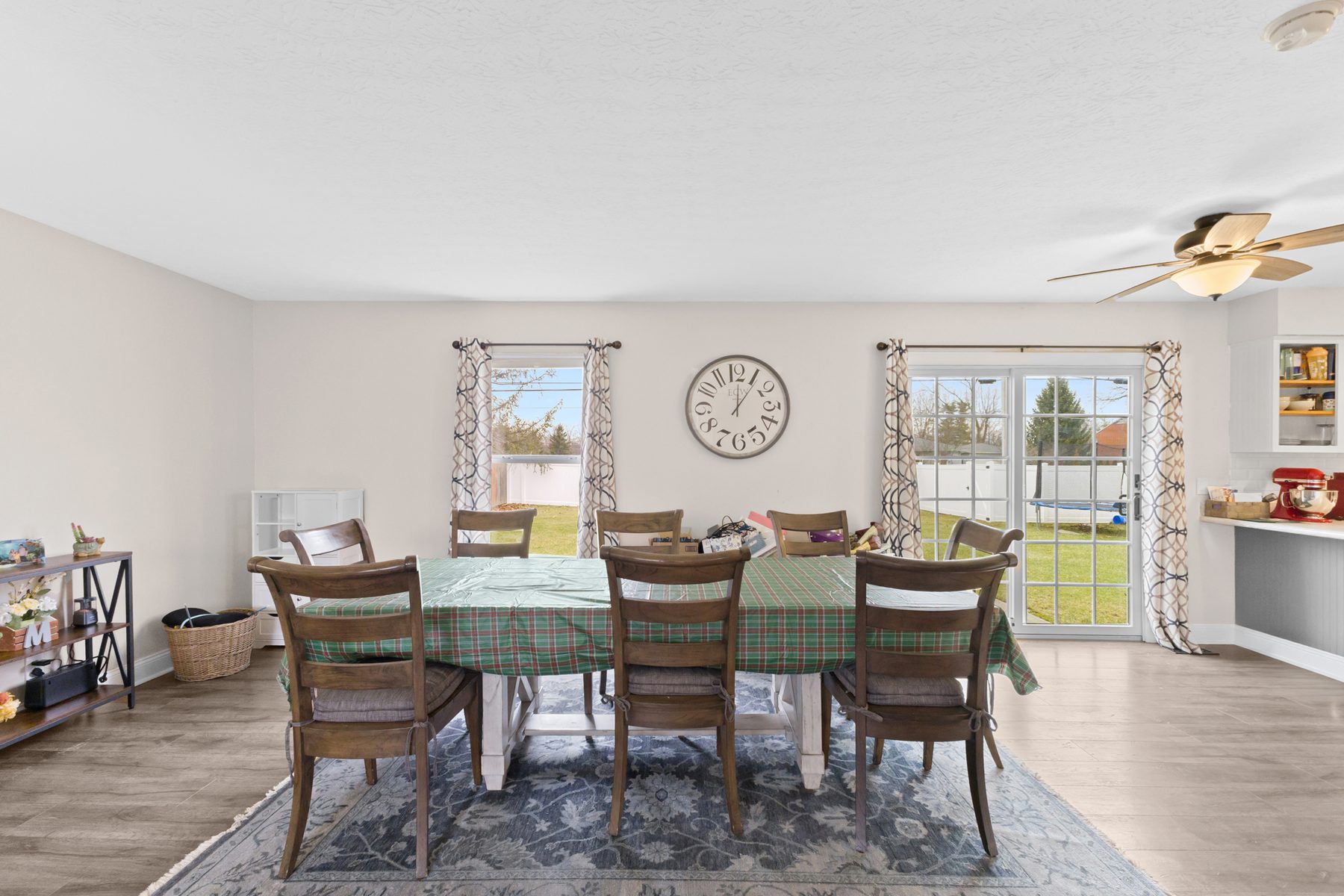 Dining area with a wood table and six chairs on a patterned rug, between two windows and doors out to the back yard