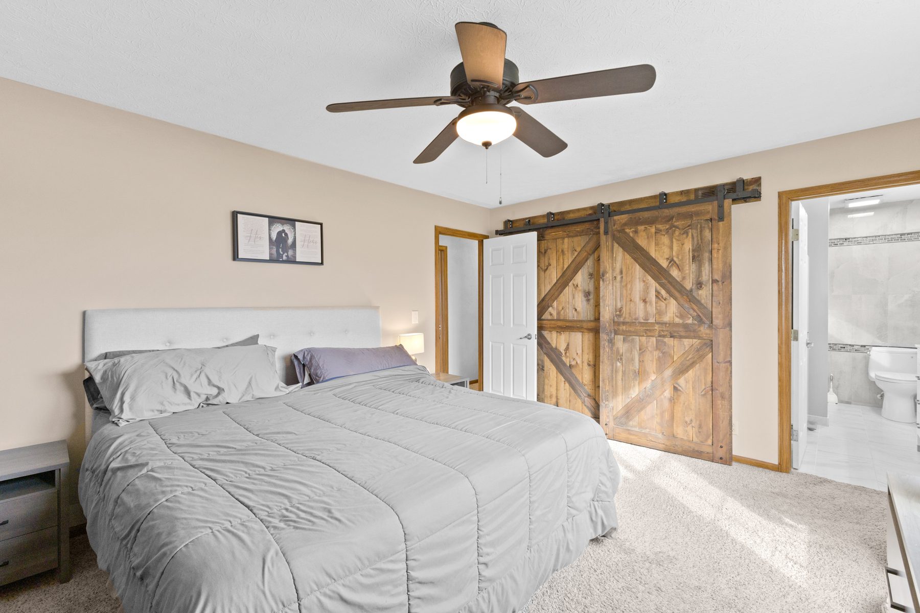 Primary bedroom with a queen bed, ceiling fan, carpeted floor and a sliding barn door to the bathroom