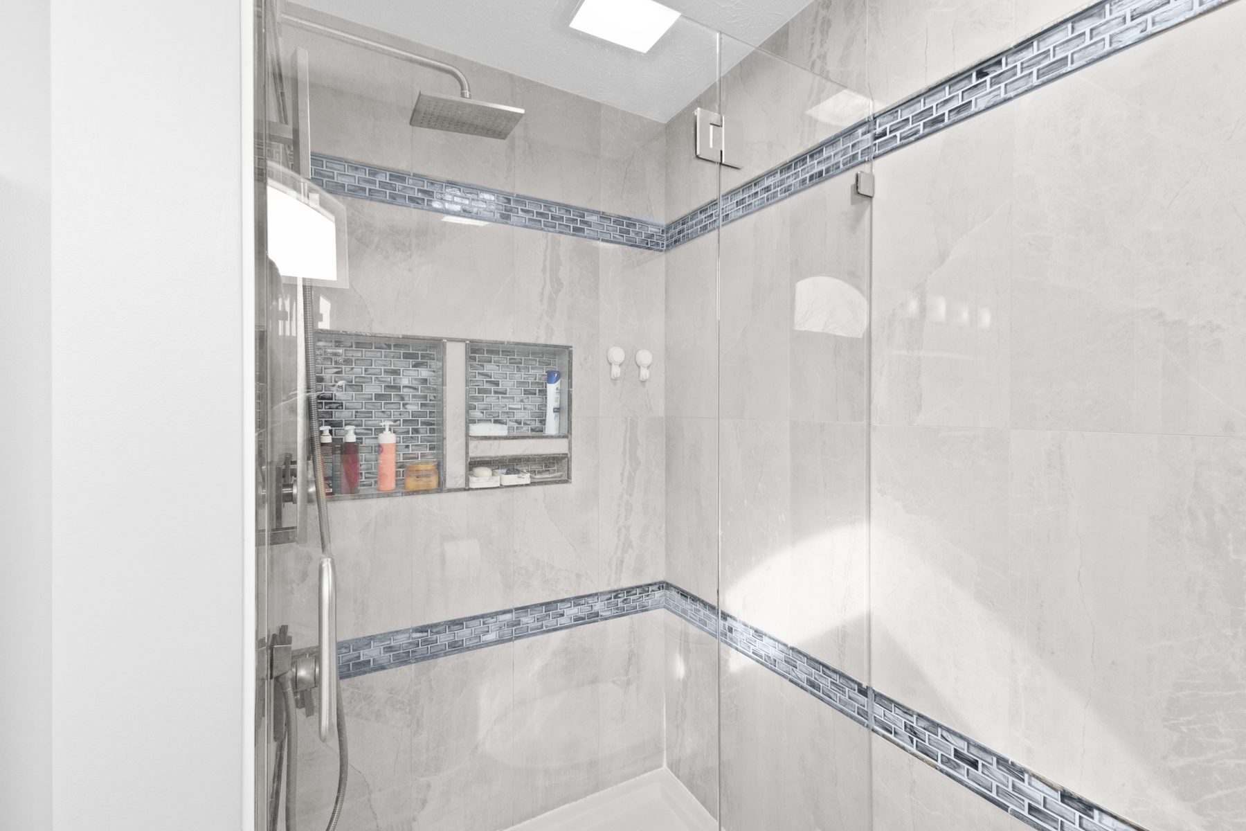 Tiled walk-in shower with a glass panel, mosaic accent bands, a recessed niche and a rain shower head
