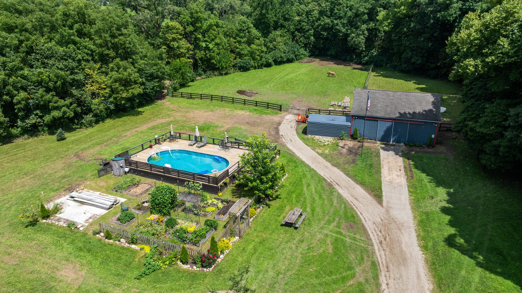 Top-down aerial of the back yard at 4933 Township Rd 164: the above-ground pool and its wraparound deck, the raised garden beds, the gravel drive and the roof of the outbuilding