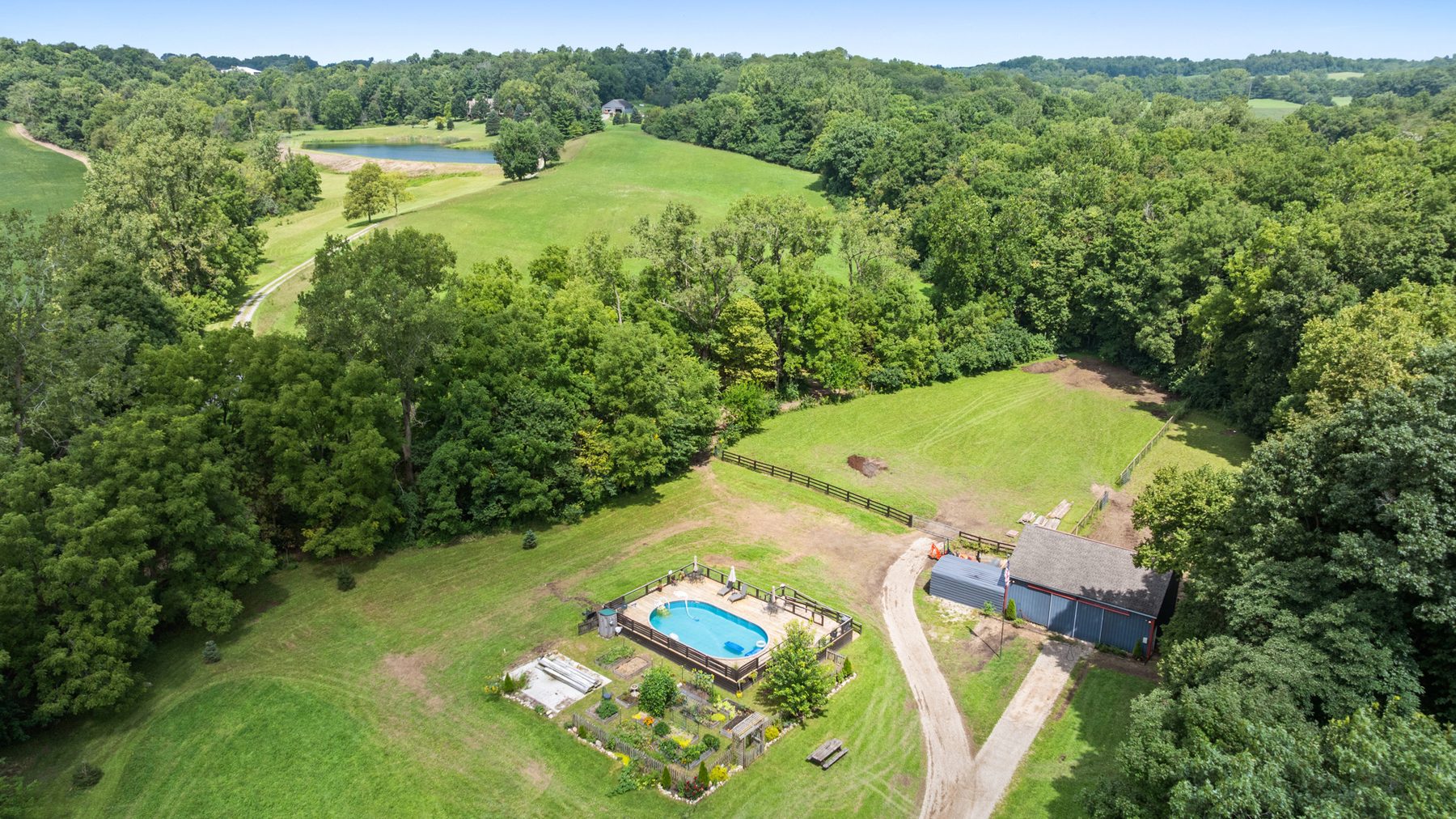 Aerial view over the acreage: rolling pasture, the tree line and a pond in the distance