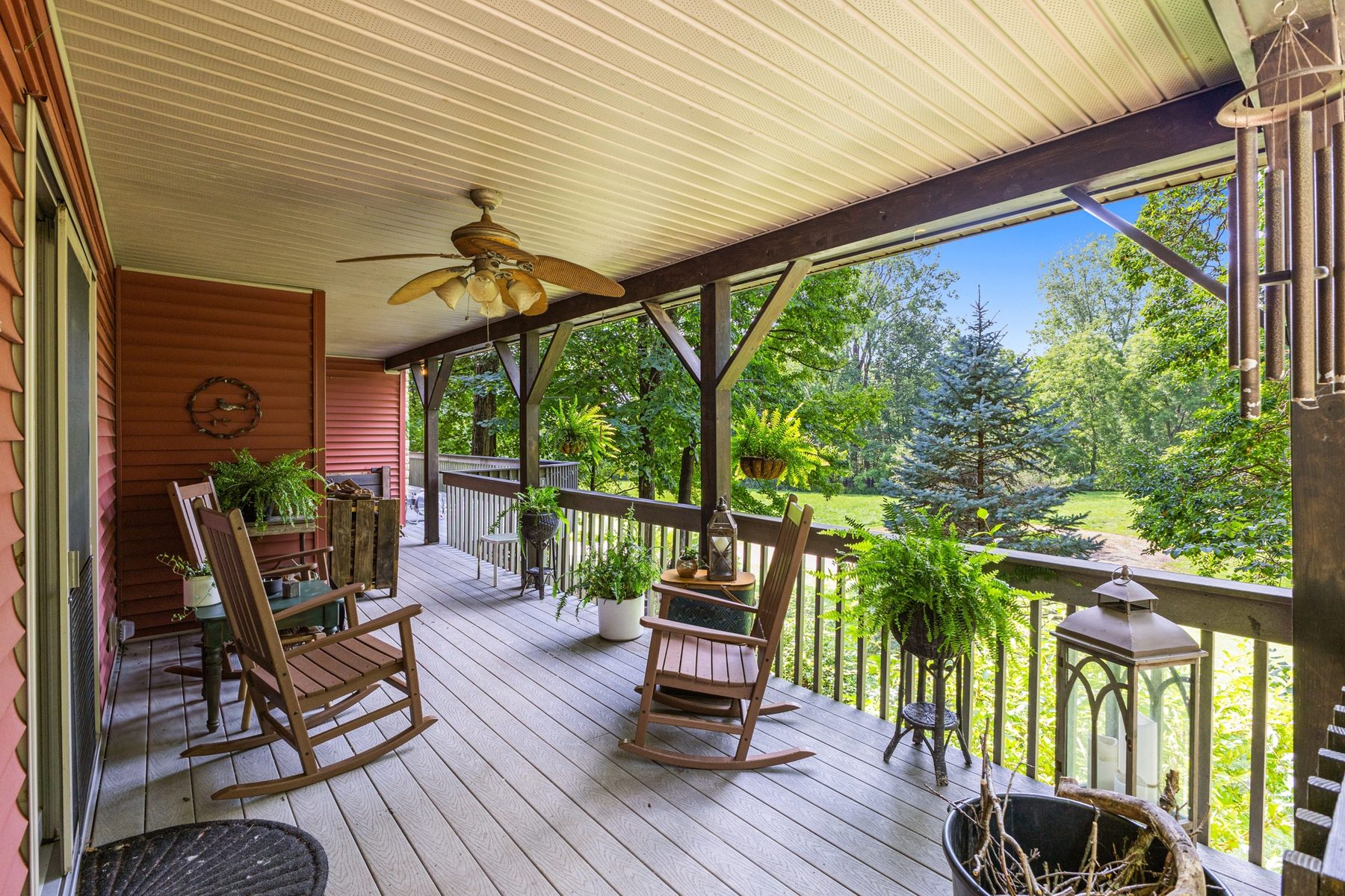 Covered porch in daylight, with rocking chairs, hanging ferns and a plank ceiling running the length of it
