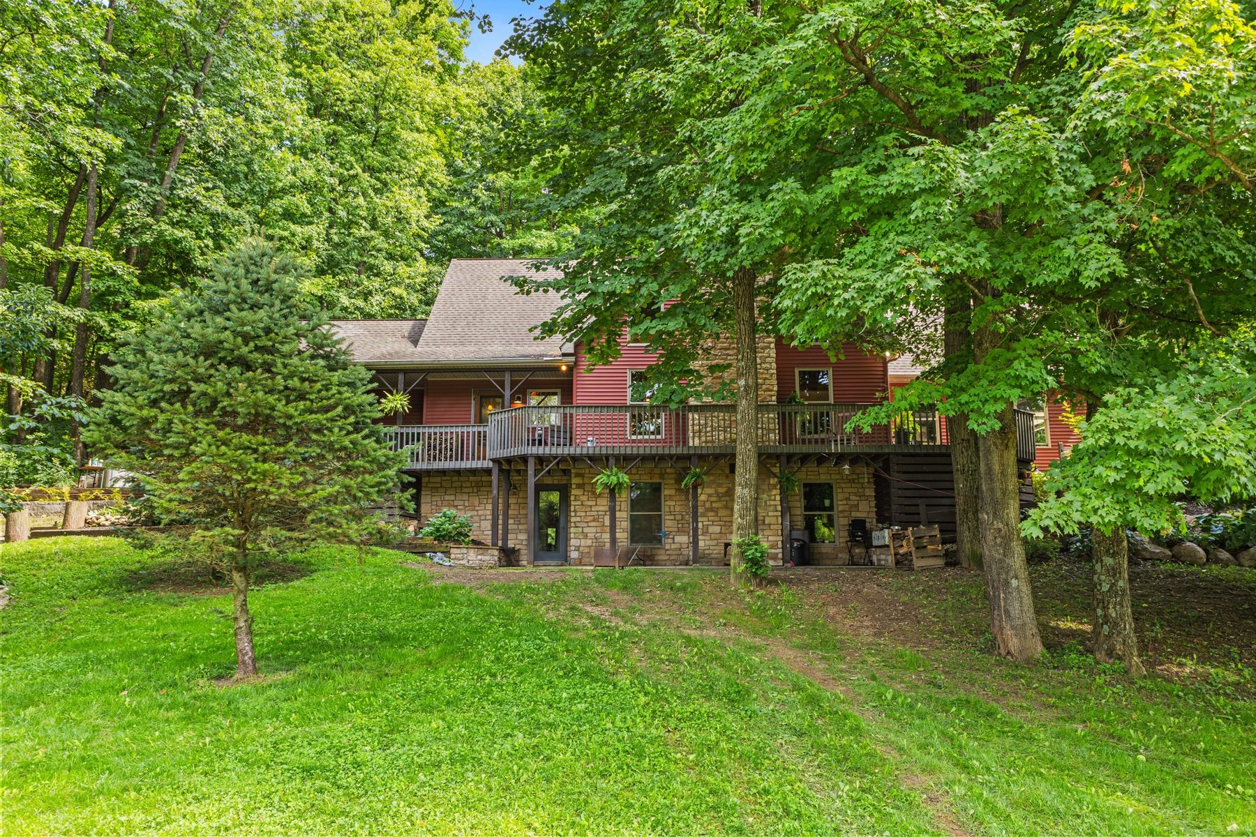 Rear of the house with the raised deck above a stone-faced lower level and lawn running up to the trees