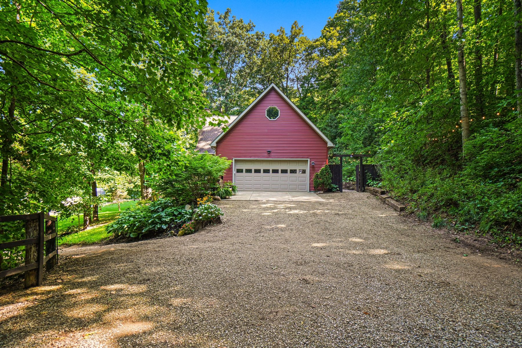 Grey-blue outbuilding with red roof trim and a garage door at the end of the gravel drive