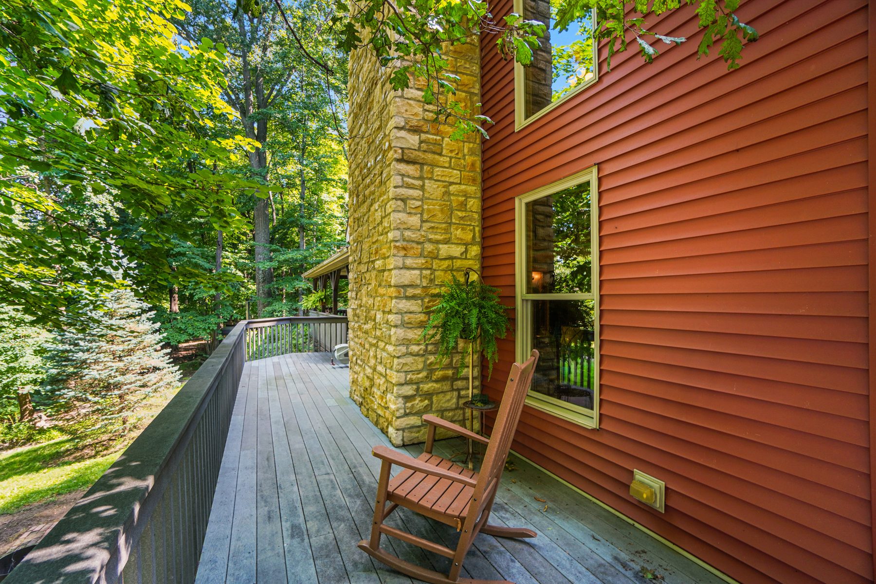 Deck running along the side of the house past the stone chimney, with a rocking chair looking out over the yard