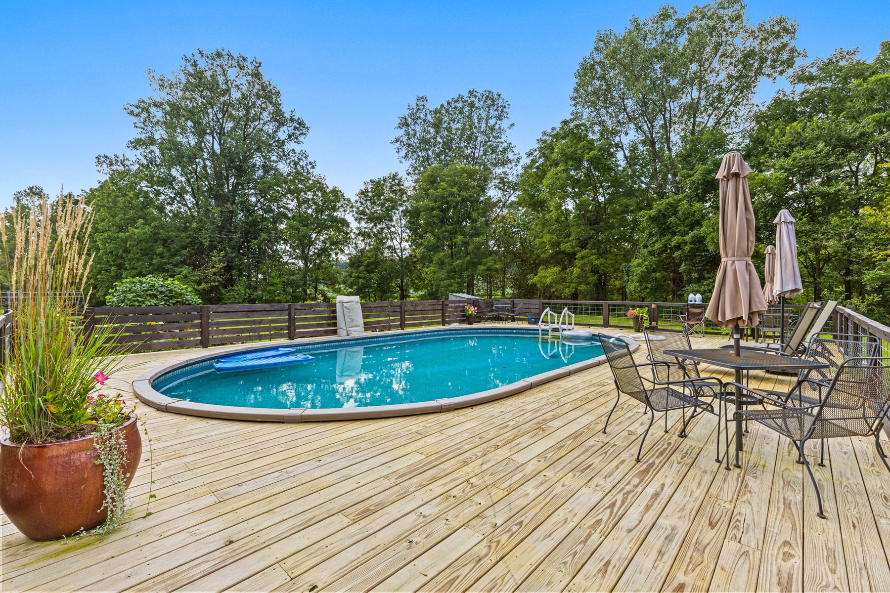 Above-ground pool with a wraparound wooden deck built up to the rim, set with a patio table, chairs and folded umbrellas