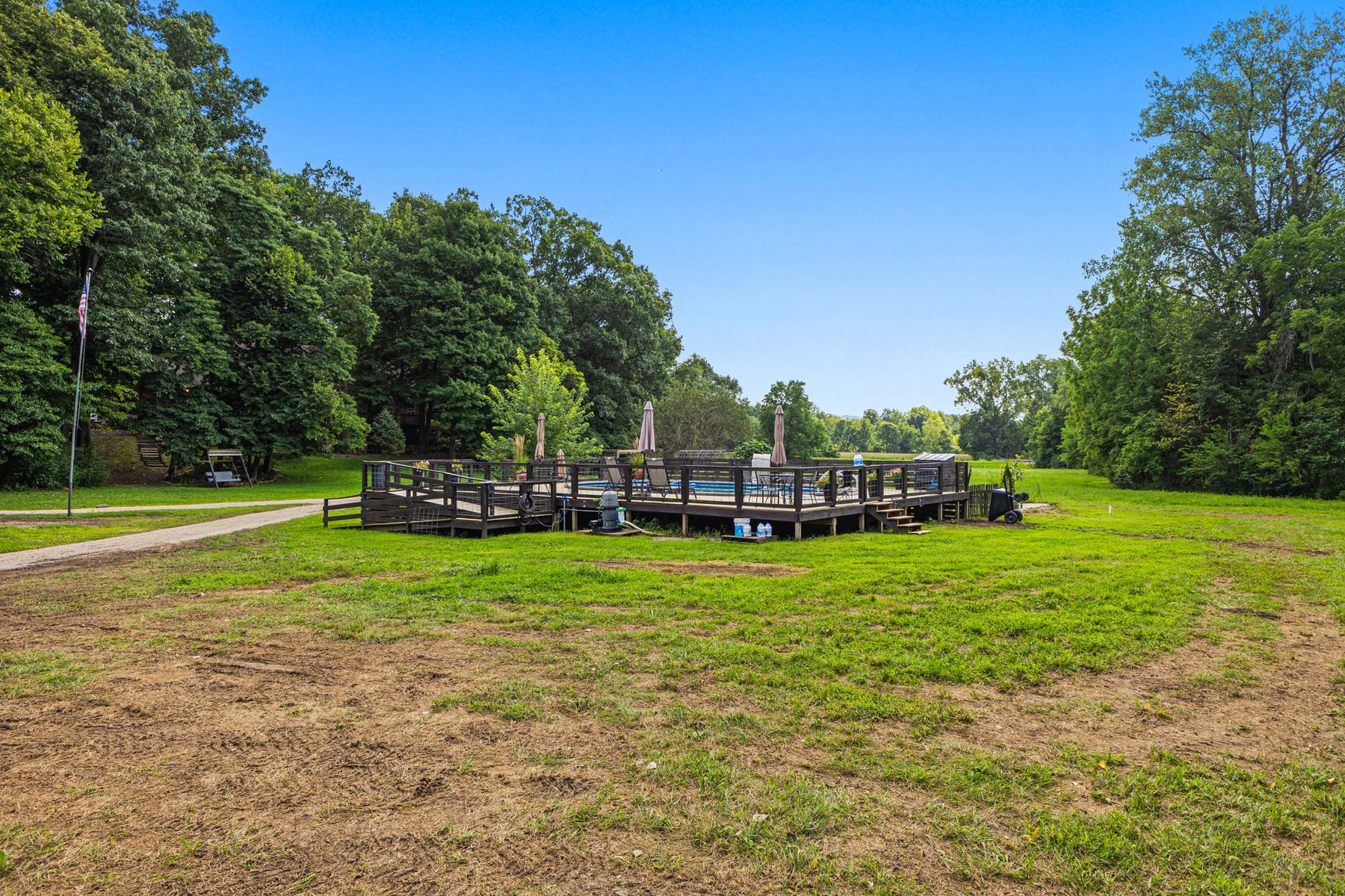 Open lawn and pasture with the pool deck at the far side and woods along the boundary