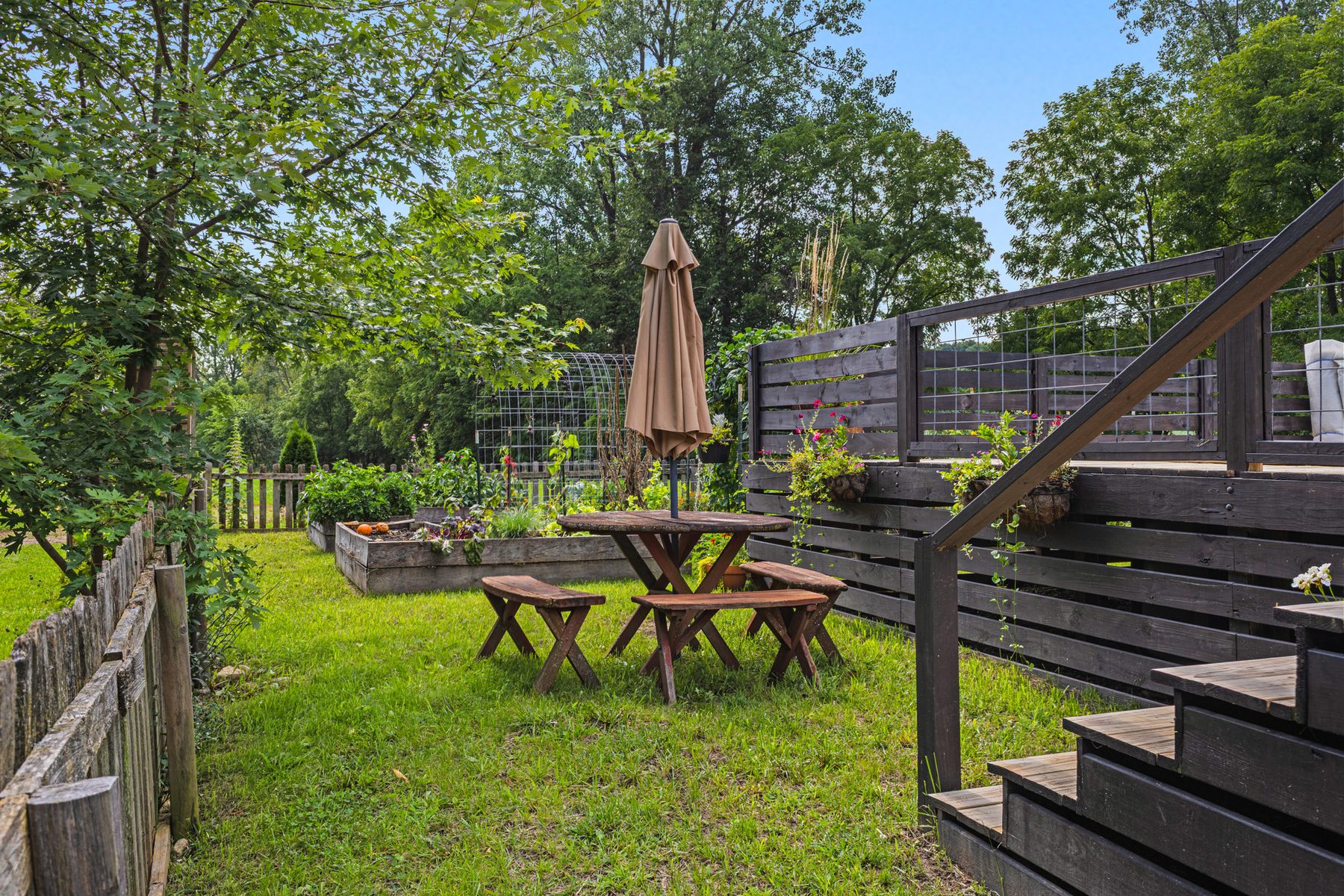 Raised garden beds and a picnic table beside the deck stairs, under a patio umbrella