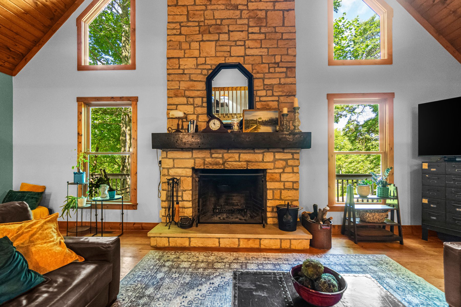 Great room with a floor-to-ceiling stone fireplace, tall windows either side and a plank cathedral ceiling