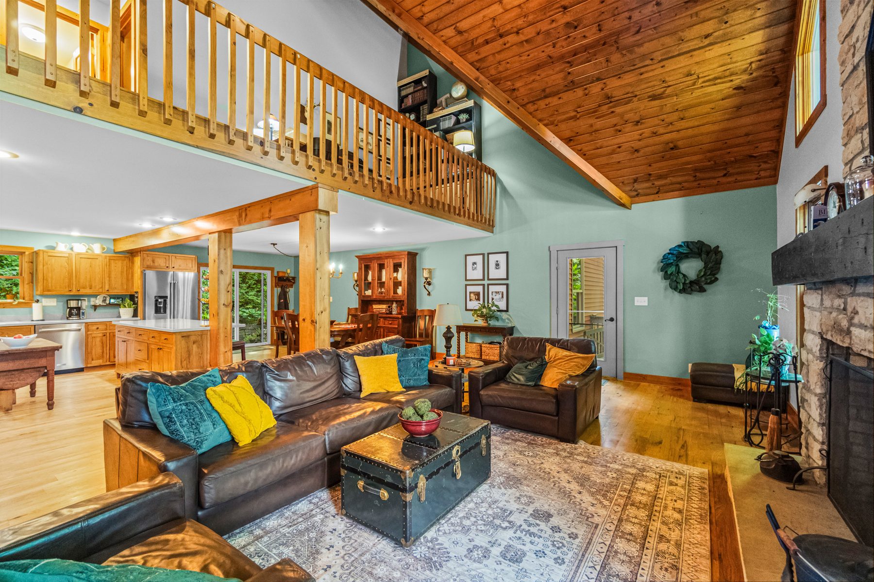 Great room from the other end, with leather seating, the stone fireplace and the open loft railing above
