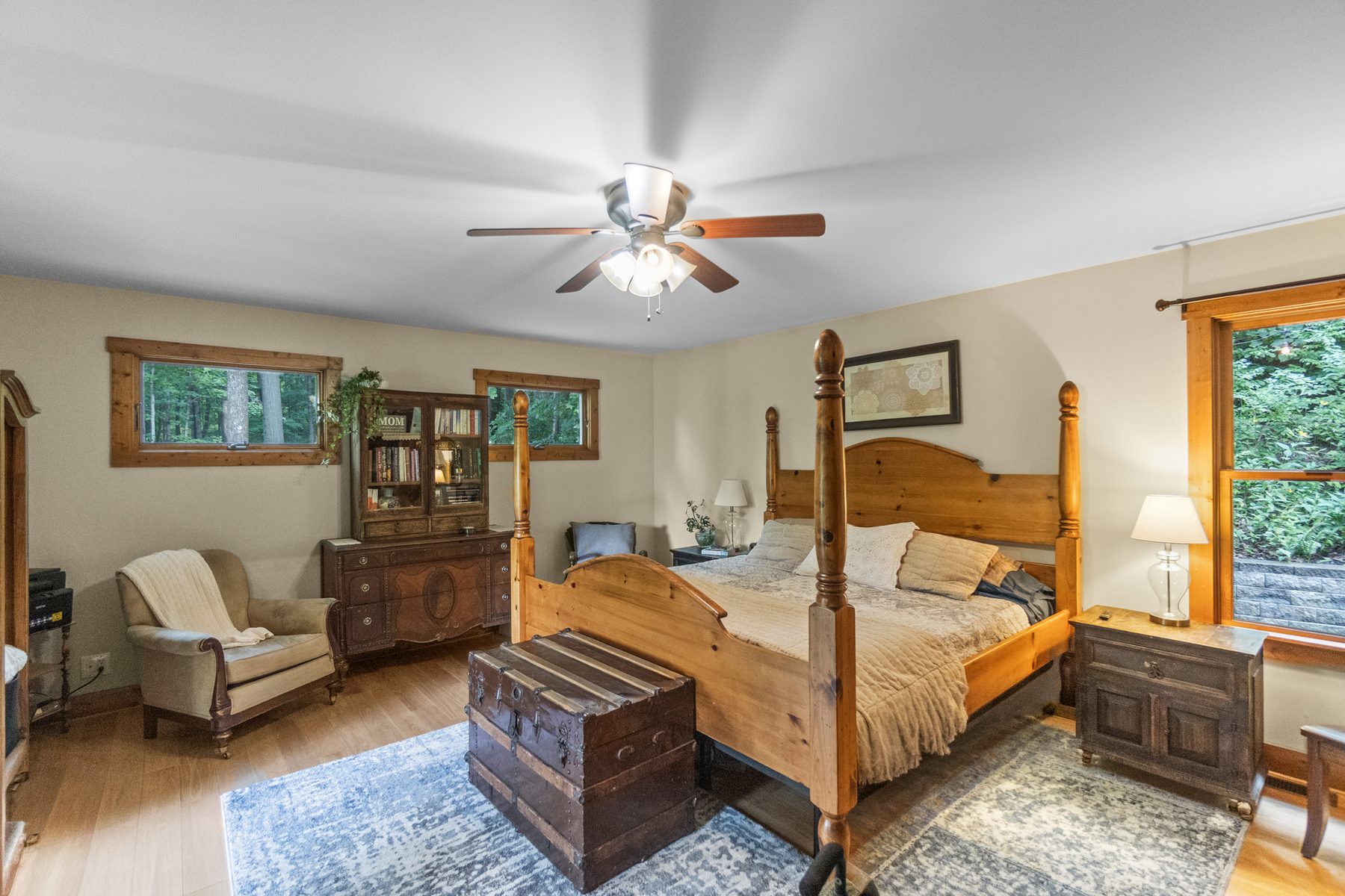 Primary bedroom with a four-poster bed, ceiling fan and windows onto the trees