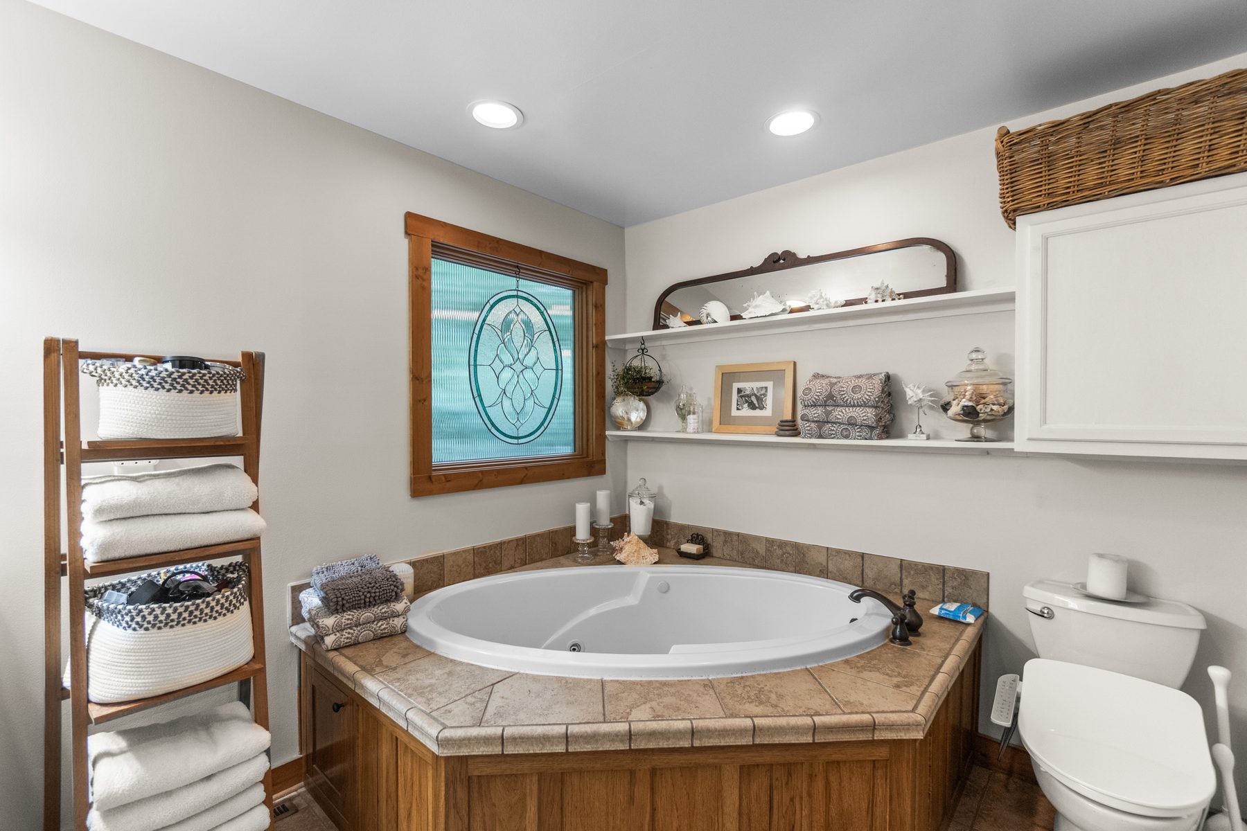 Primary bathroom with a tiled jetted garden tub below a leaded-glass window and a shelved linen ladder