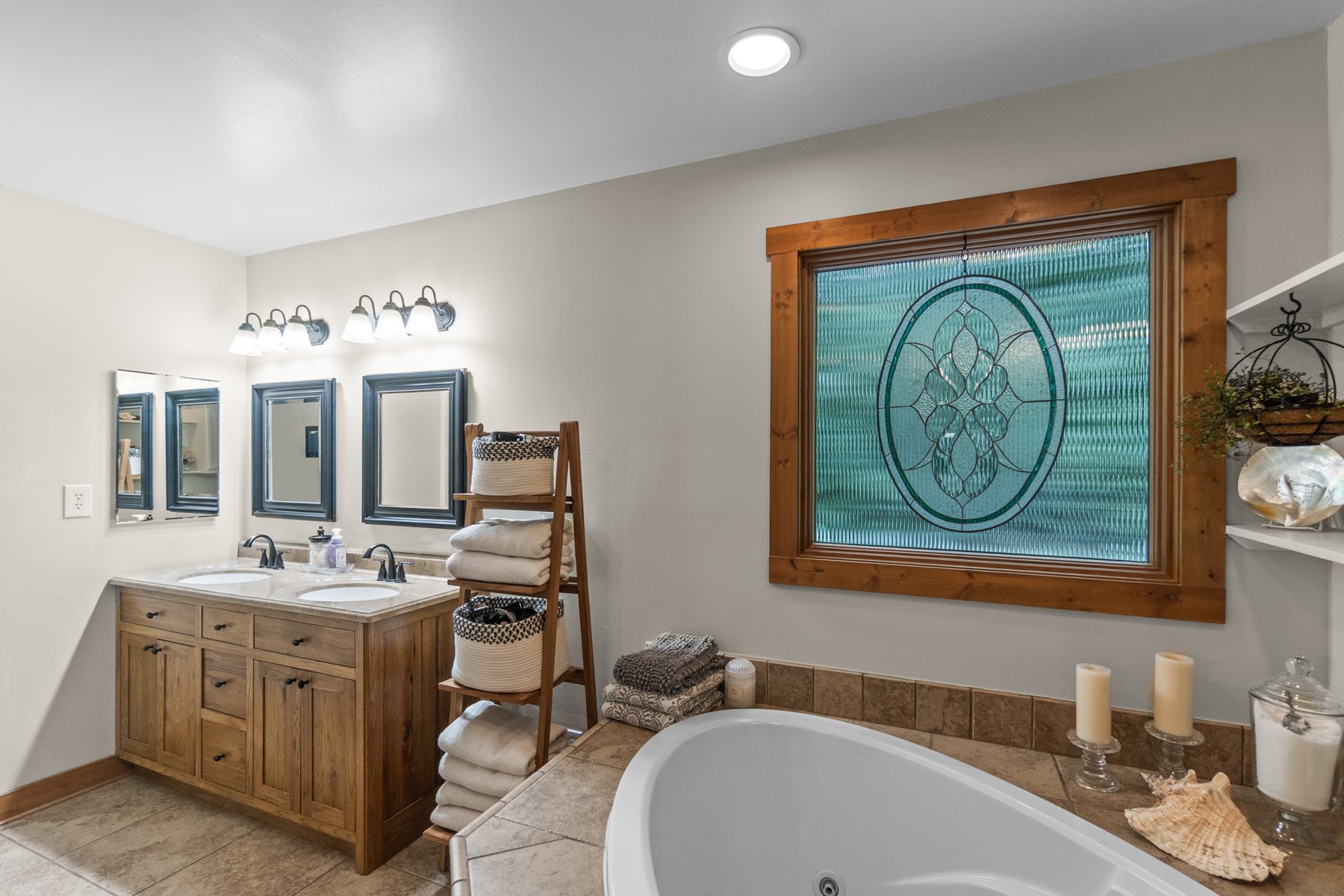 Bathroom vanity with two sinks, framed mirrors and a soaking tub beneath the leaded-glass window