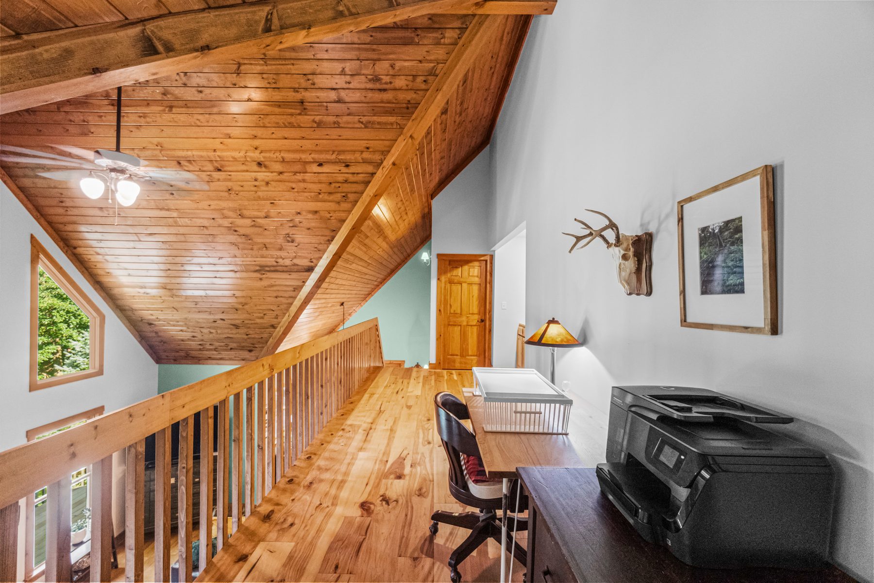 Open loft under a plank cathedral ceiling, railed above the great room and set up as a work space
