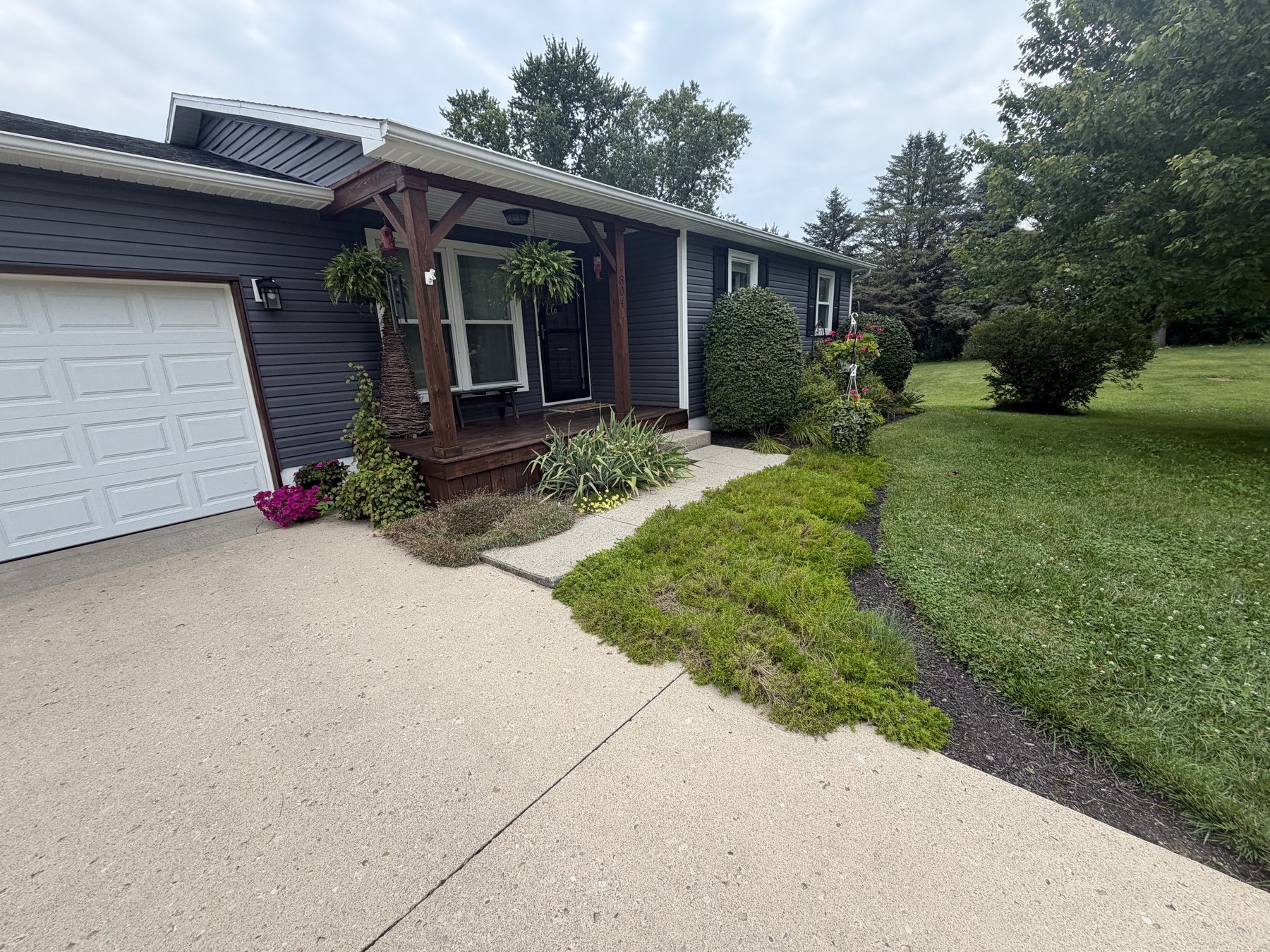 Front walk and attached garage seen along the driveway, with planting beds and mown lawn either side