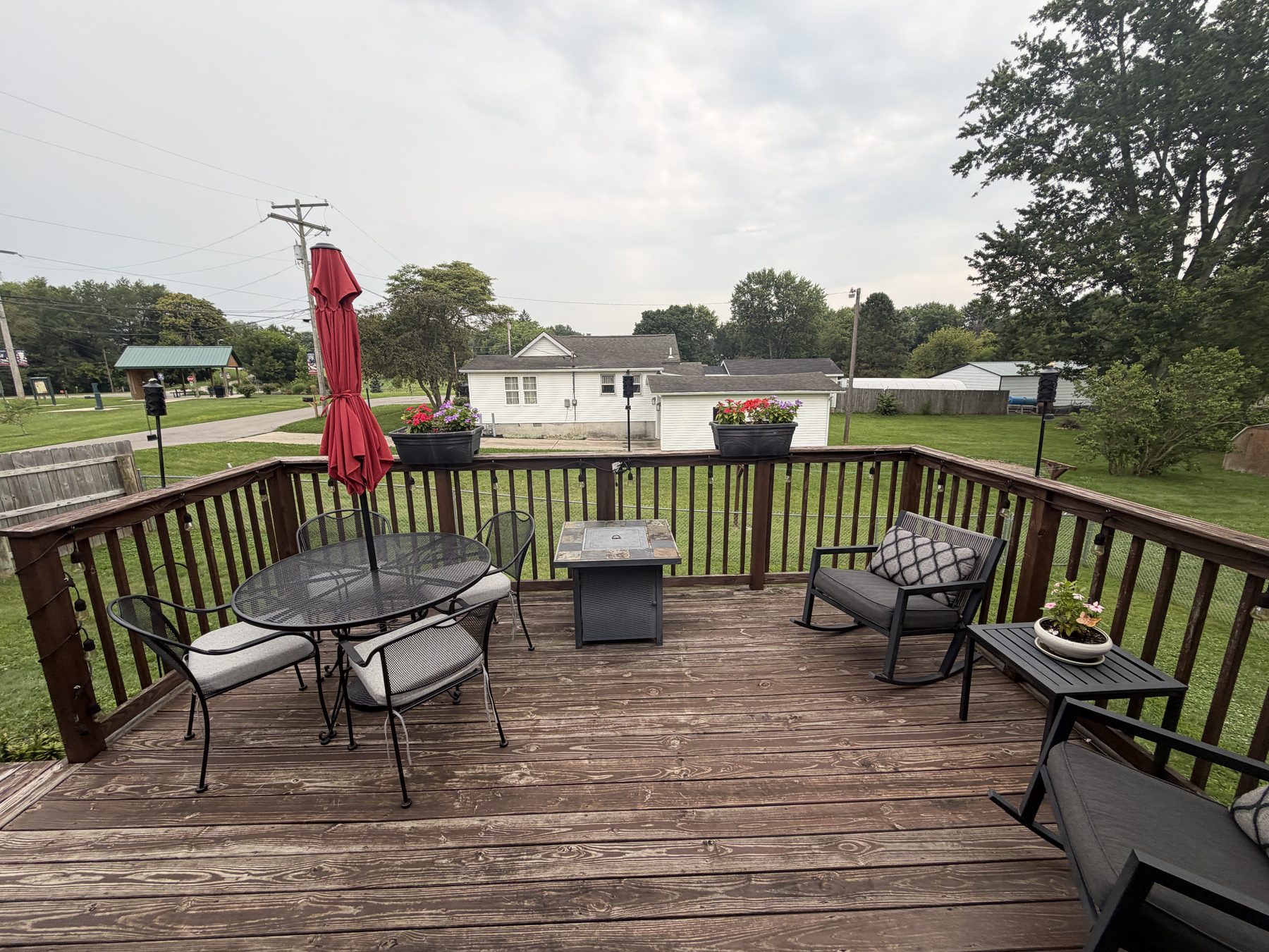 Raised wood deck at the back of the house with a patio table and chairs, a folded red umbrella and the back yard beyond the railing