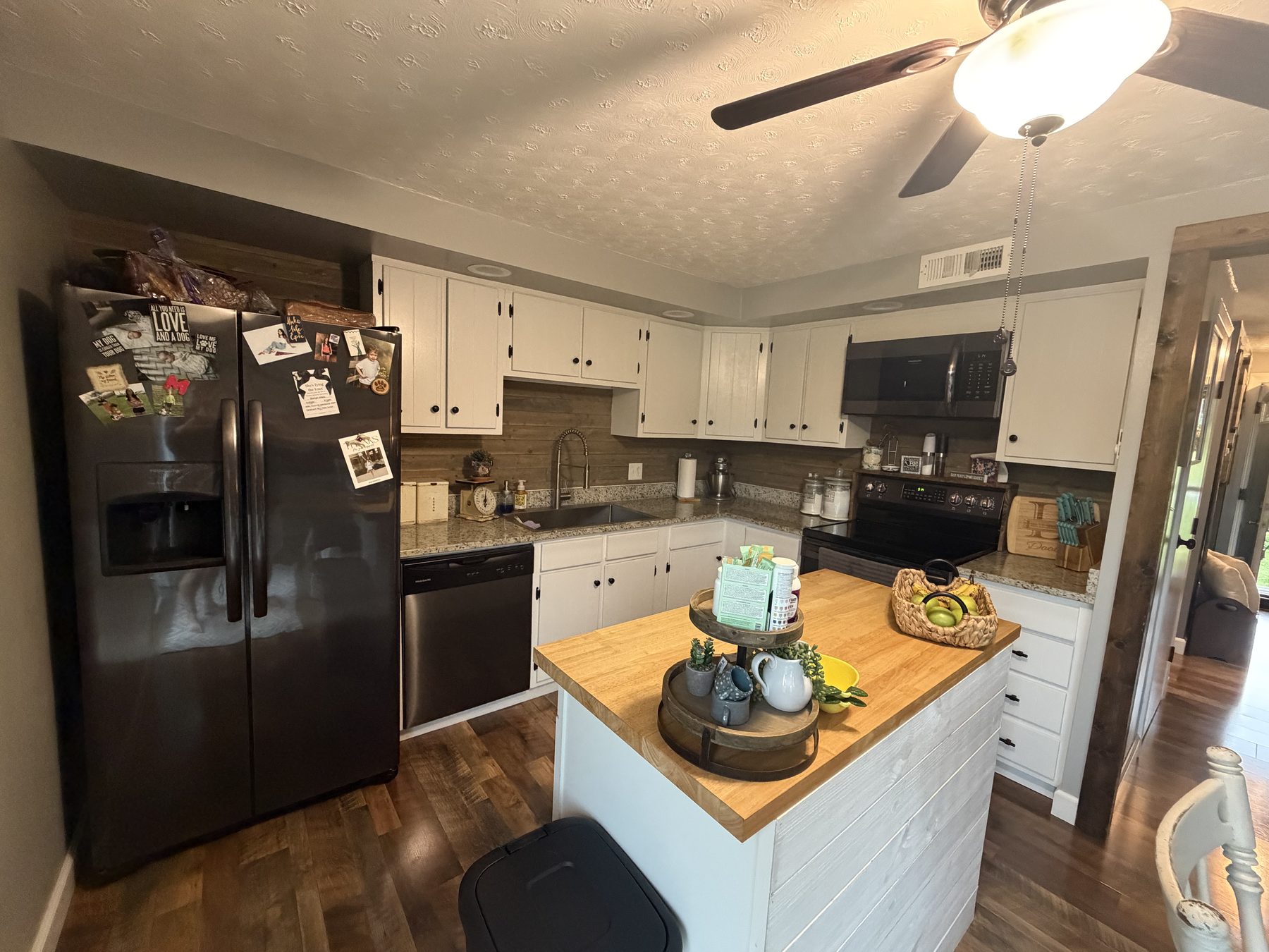 Kitchen with white cabinetry, granite counters, a butcher-block-topped island, a black refrigerator and a black range