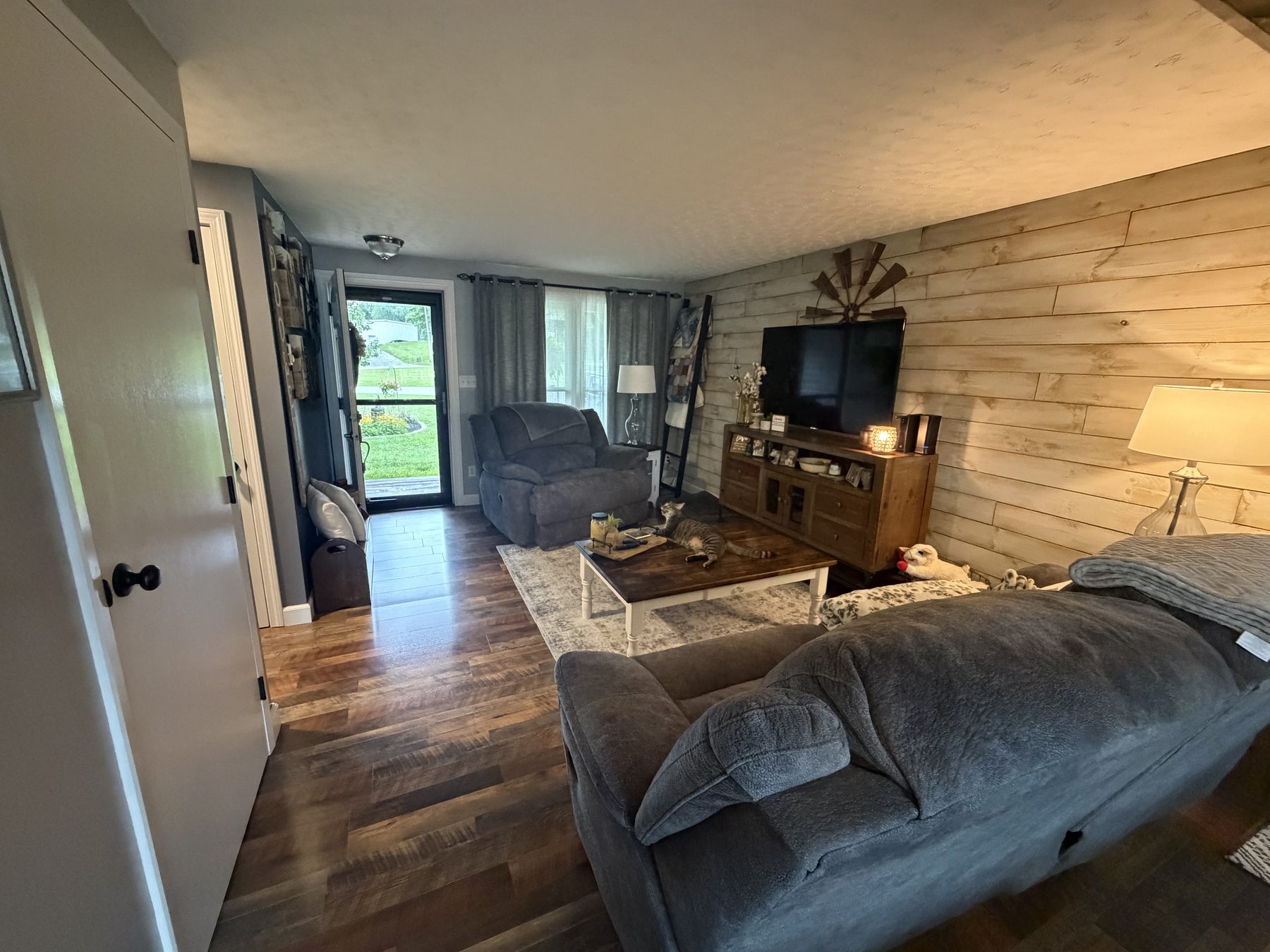 Living room with a wood plank accent wall, dark plank flooring, seating and a television on a wood console beside a sliding door